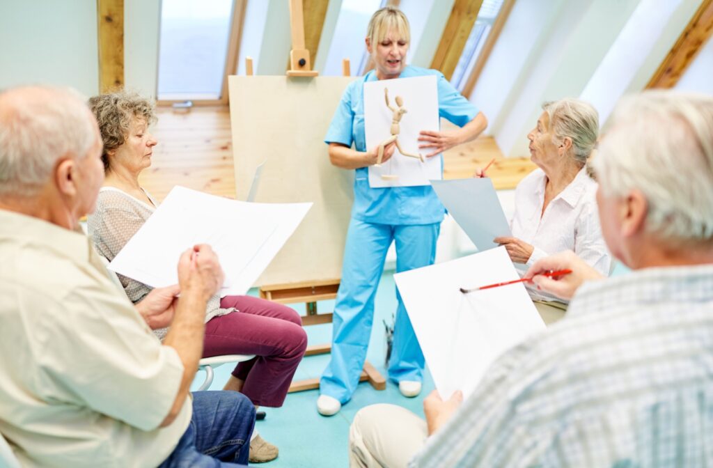  An art therapist in blue scrubs teaches a class to a group of seniors with dementia in a well-lit room in memory care